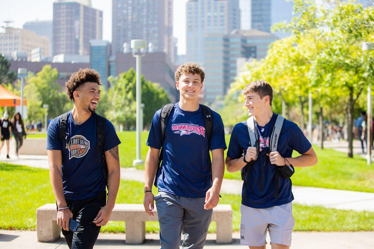 Three students standing together in front of greenery and the Denver skyline.